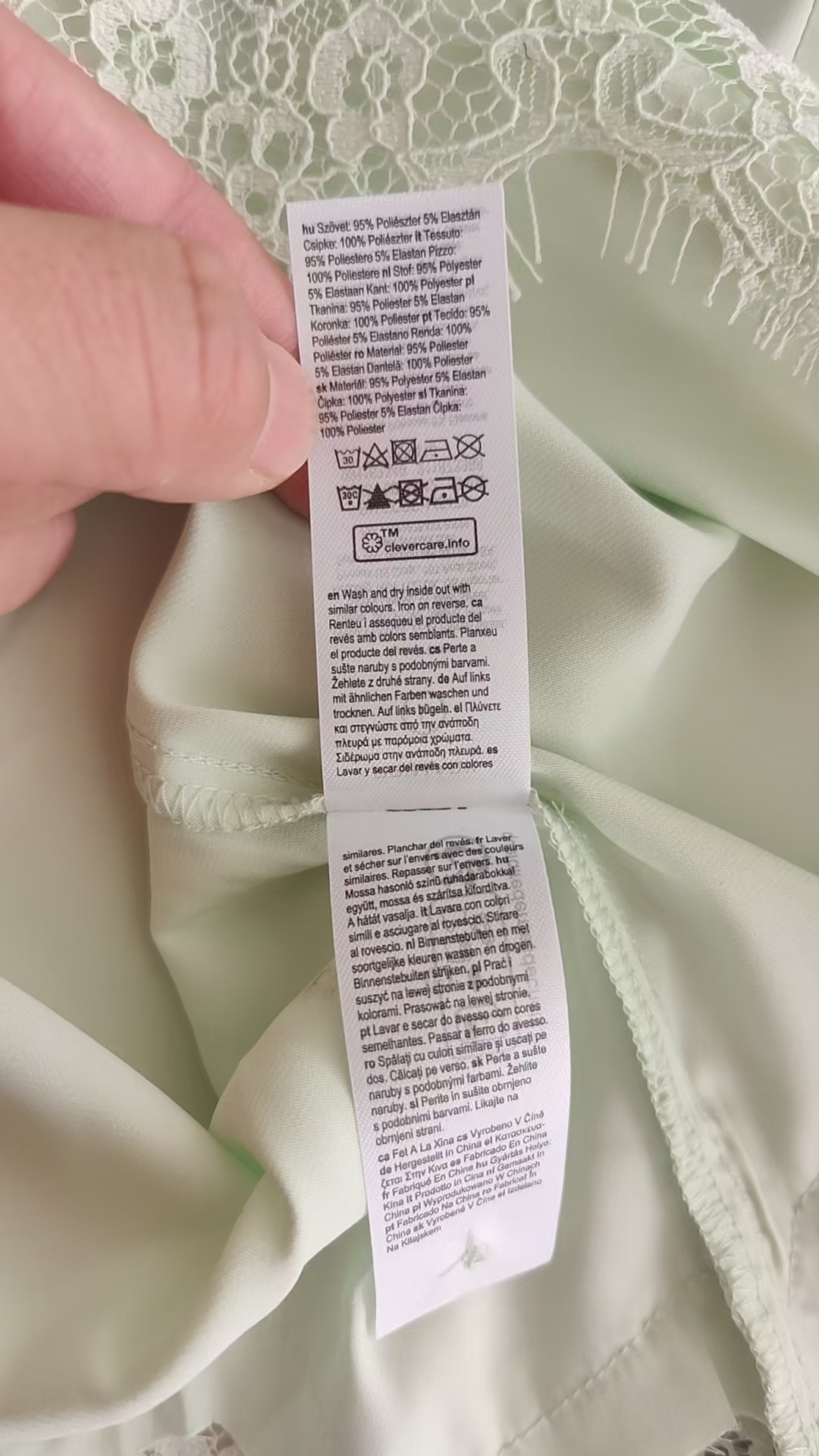 Close-up detail of light green blouse neckline showing lace trim and brand label