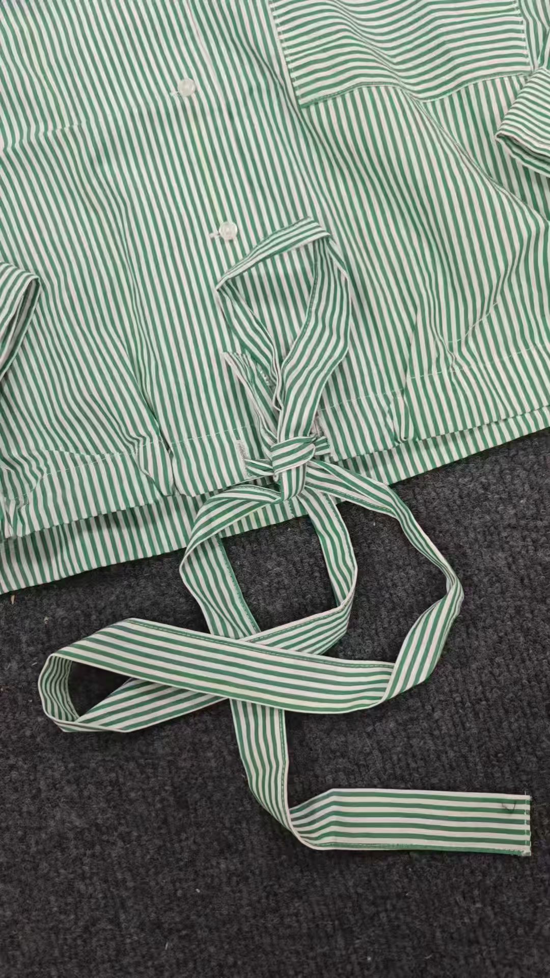 Close-up detail of green striped blouse sleeve cuff and side tie knot