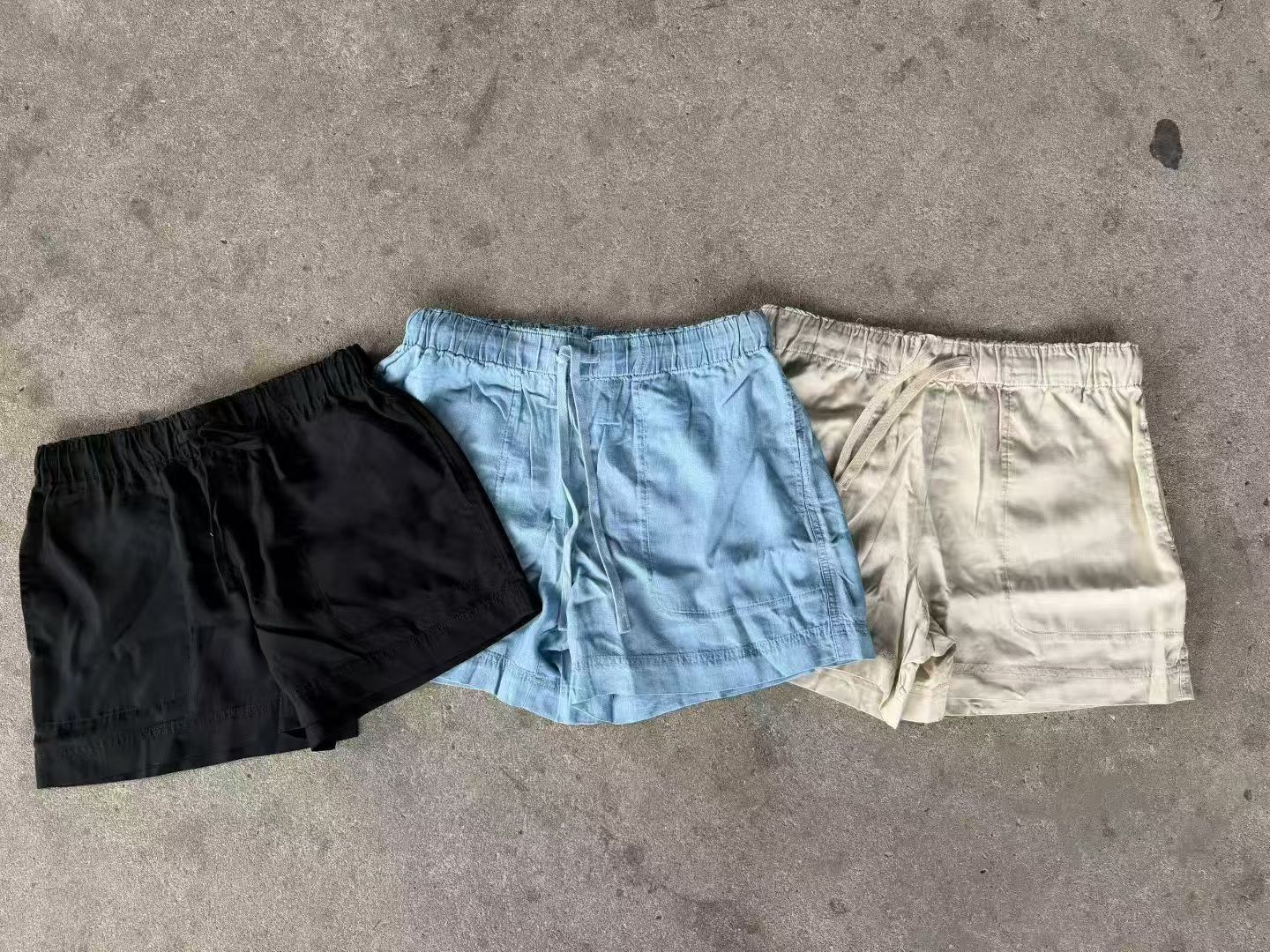Three pairs of women's Tencel shorts in black, light blue, and off-white laid flat on a light-colored surface.