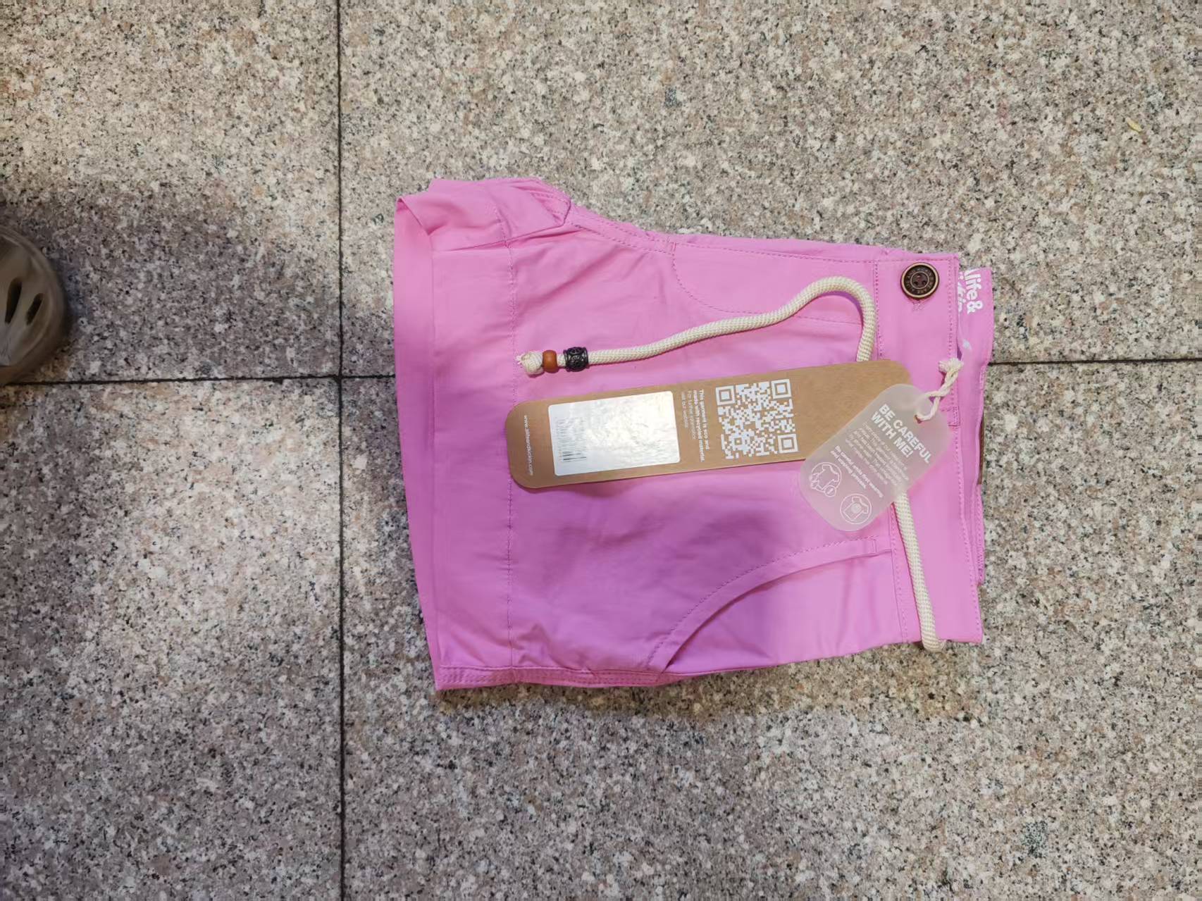Pink women's casual shorts laid flat on floor, including packaged items and label details.
