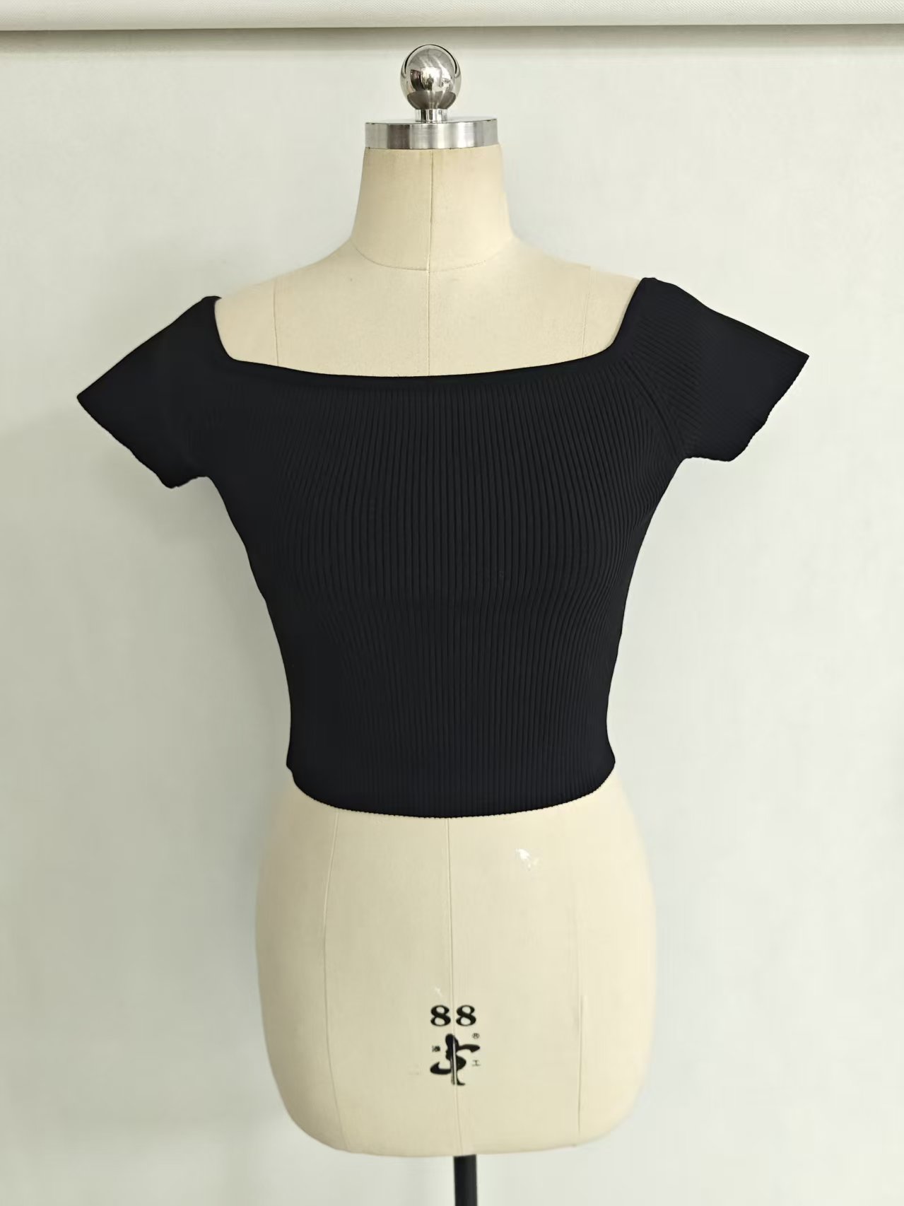 Women's ribbed off-the-shoulder crop top in black displayed on a torso mannequin.