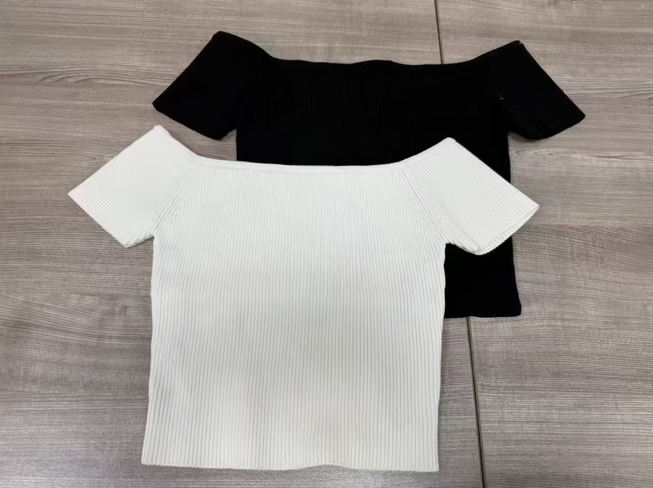 Black and white women's ribbed off-the-shoulder crop tops laid flat side by side.