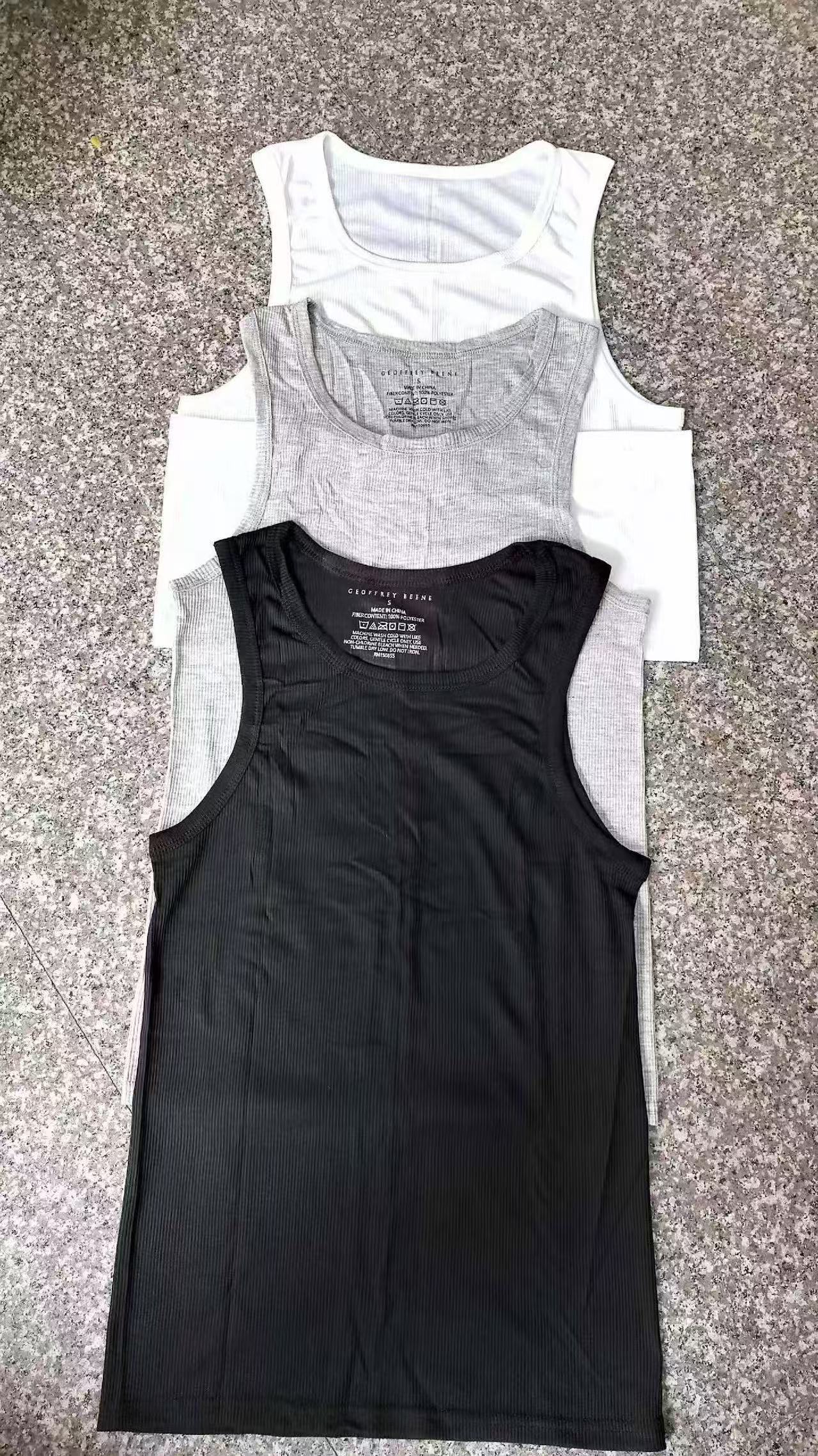 White, grey, and black men's tank tops stacked together on a flat surface.