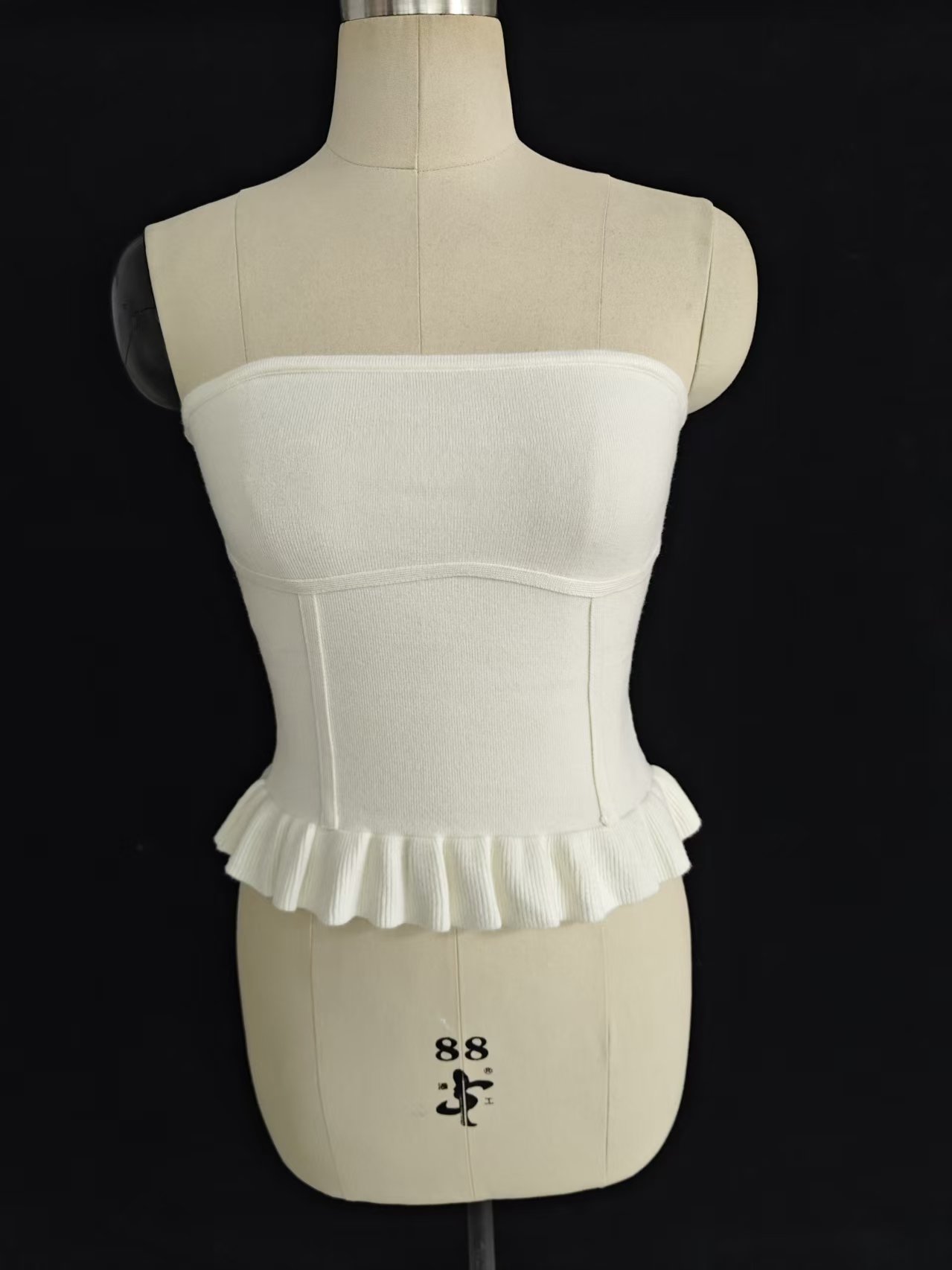 Women's white strapless tube top with ruffled hem, displayed on a torso mannequin.