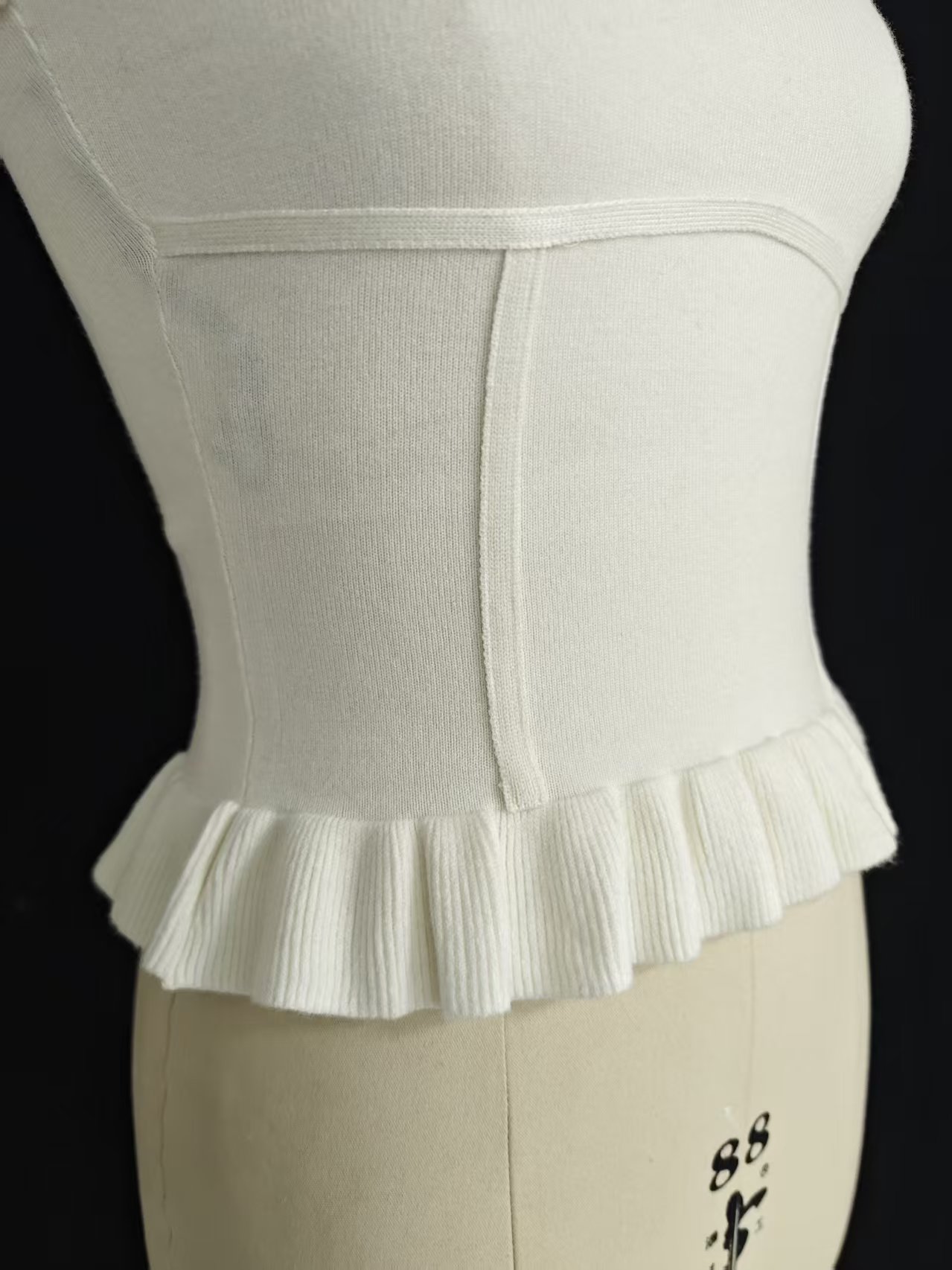 Close-up of white women's strapless tube top on a mannequin, highlighting ribbed fabric texture and ruffled trim.