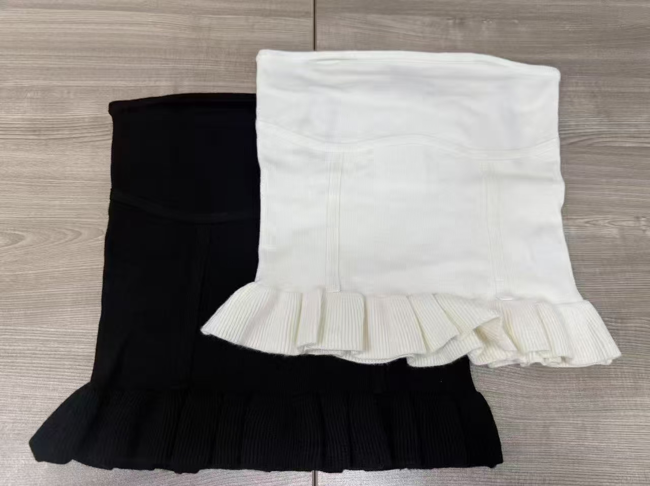 Black and white women's strapless tube tops with ruffled hem laid flat side by side.
