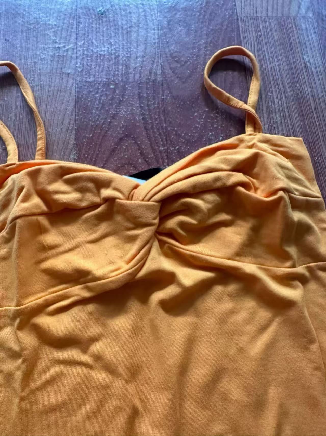 Close-up of orange women's ribbed camisole top with thin spaghetti straps laid flat.