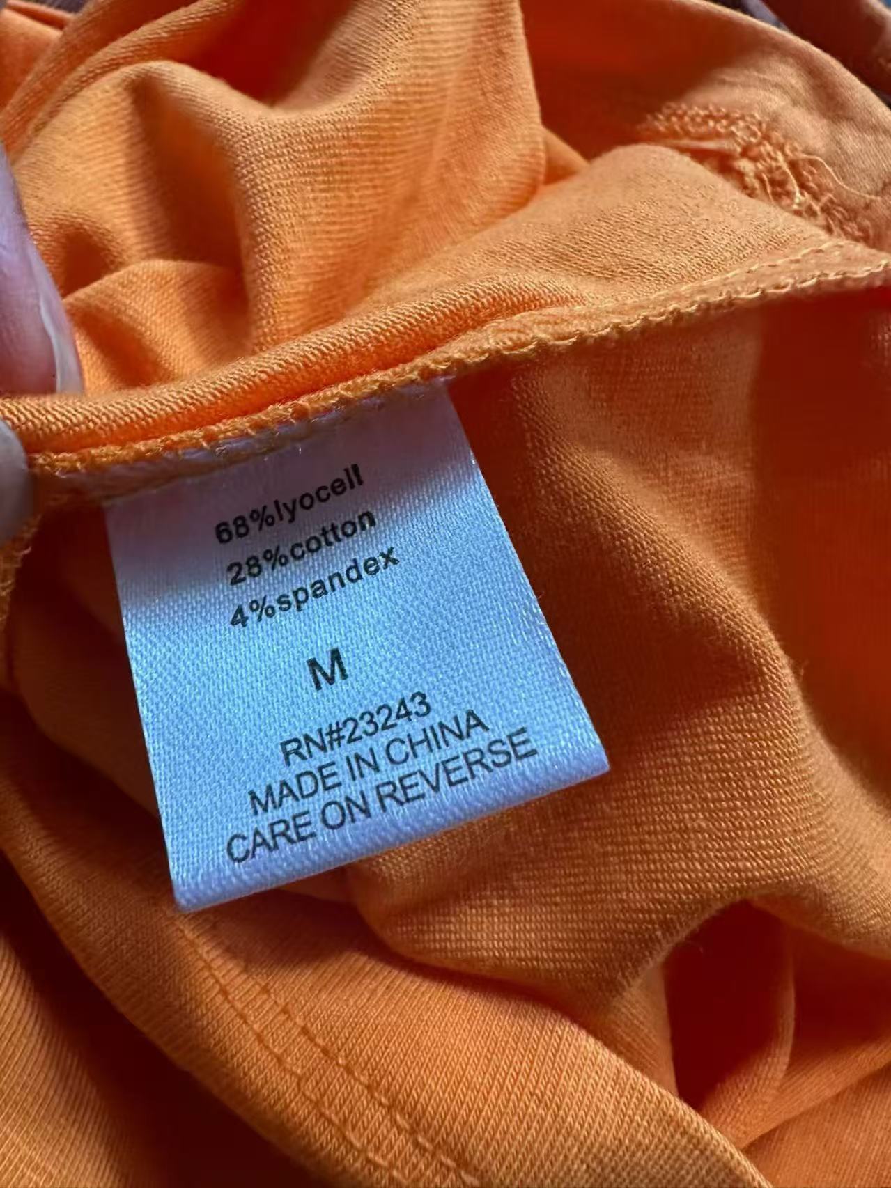 Close-up of orange women's camisole top highlighting collar line, thin strap detail, and inner brand label.