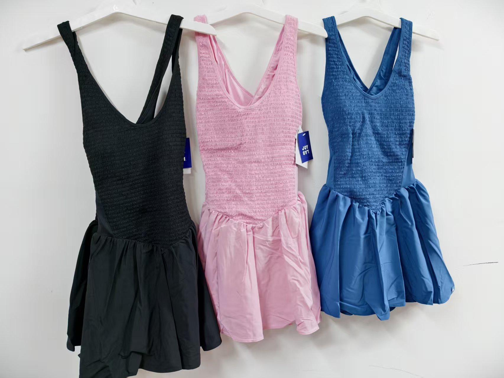 Women's athletic tennis dresses with crisscross straps in black, pink, and bright blue stacked side by side.