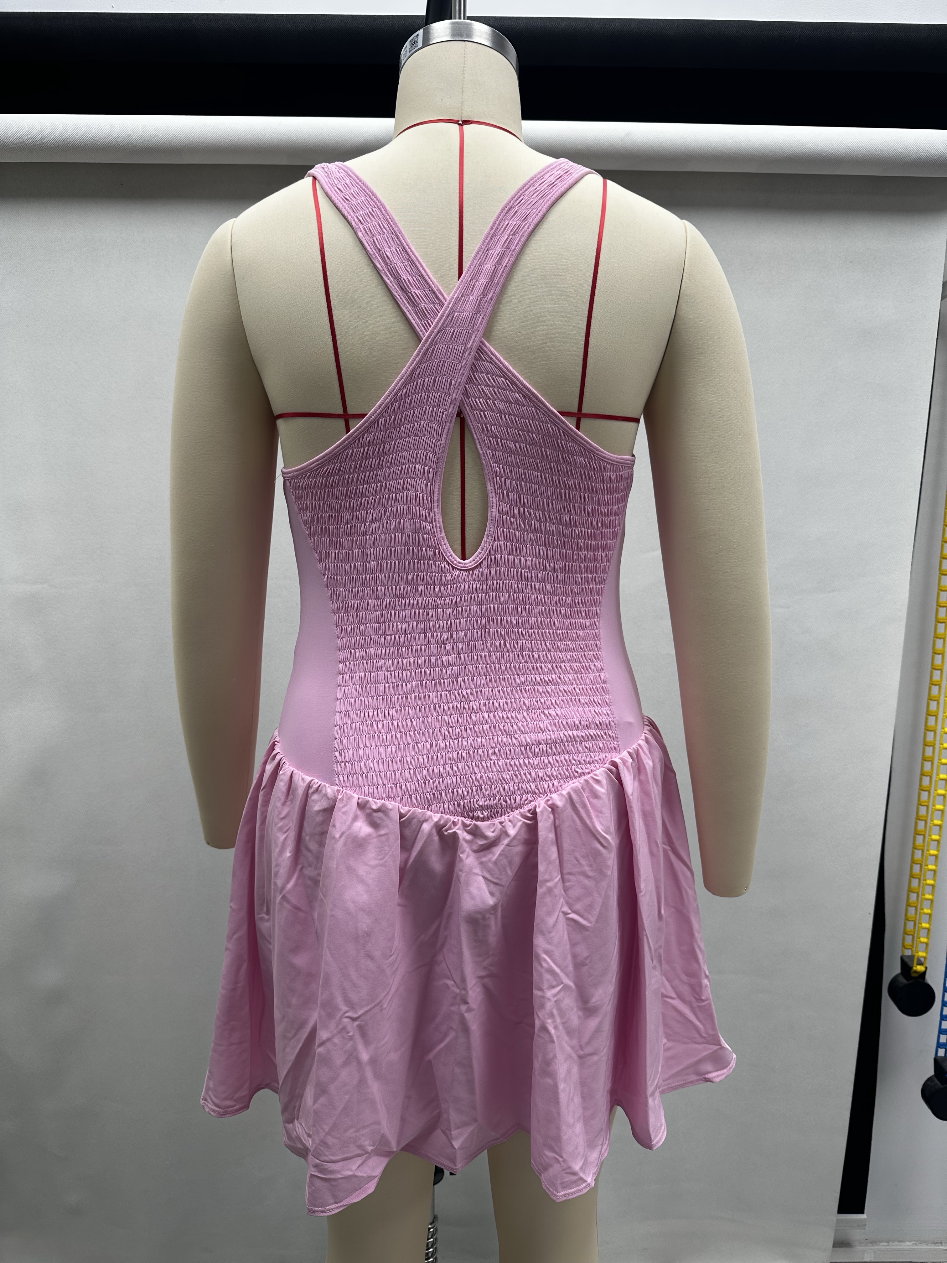 Back view of pink women's athletic tennis dress displayed on a torso mannequin highlighting the crisscross strap detail.