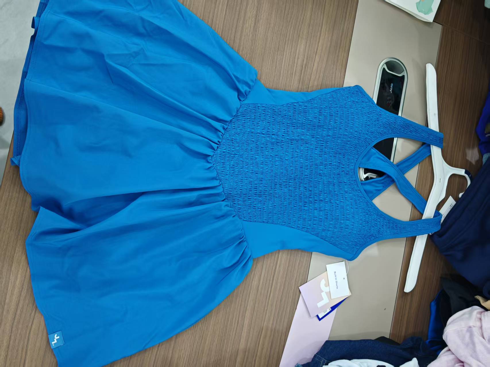 Bright blue women's athletic tennis dress with adjustable thin shoulder straps laid flat on a light-colored surface.