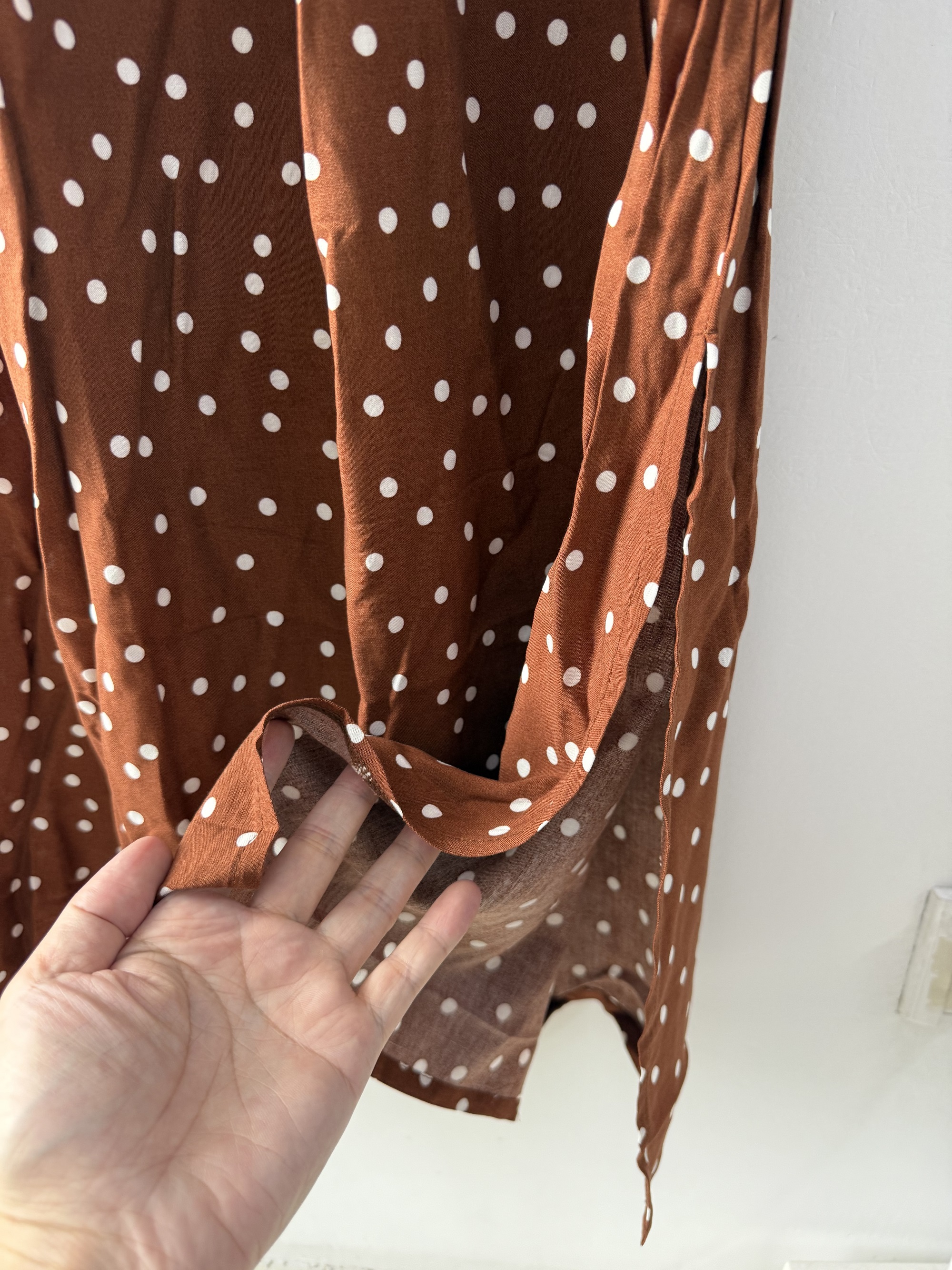 Close-up detail shot of the rust brown women's dress showing fabric texture, sheer sleeve, and white polka dot pattern.