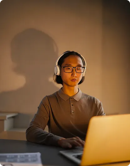 A person in headphones working at a laptop in a quiet amber-lit workspace