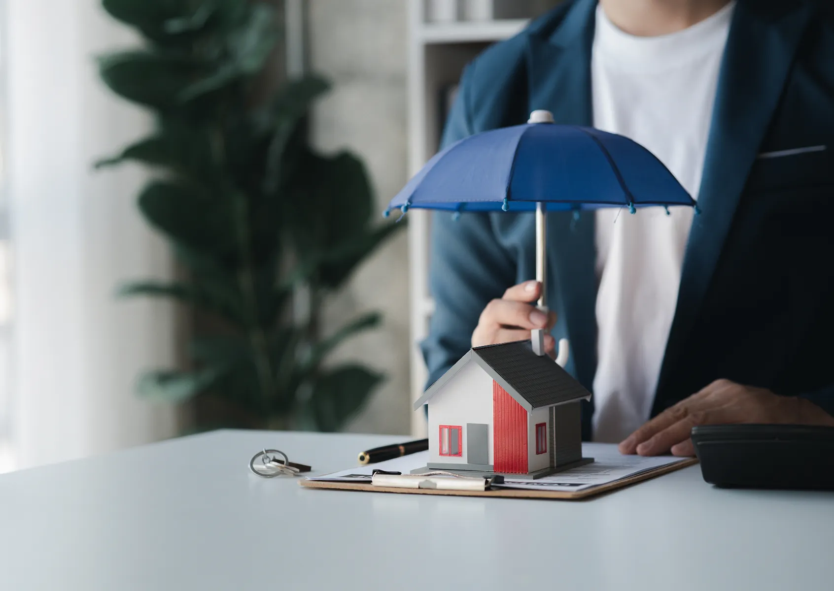 Reference Data Model Insurance section image Hand holding a small umbrella over a model house on insurance paperwork