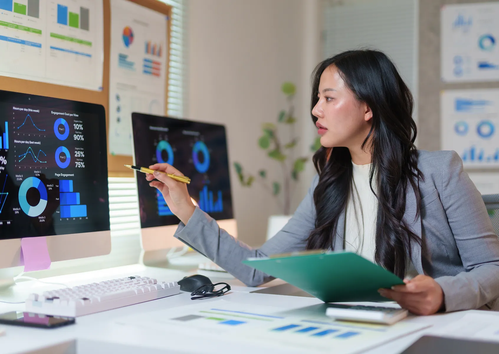 Business analyst reviewing data dashboards on two monitors while holding a report folder