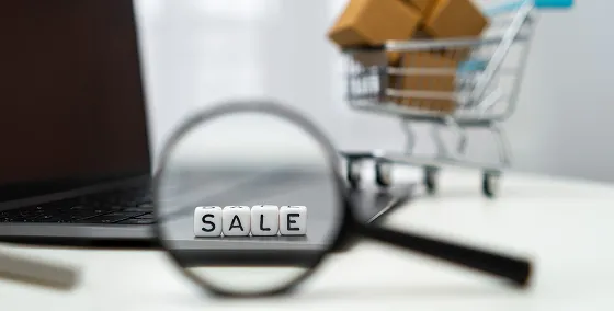 Magnifying glass highlighting a sale label beside a shopping cart and laptop.