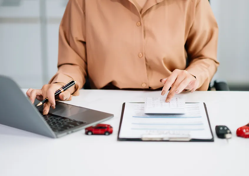 Insurance professional reviewing policy documents with a laptop and model cars on a desk