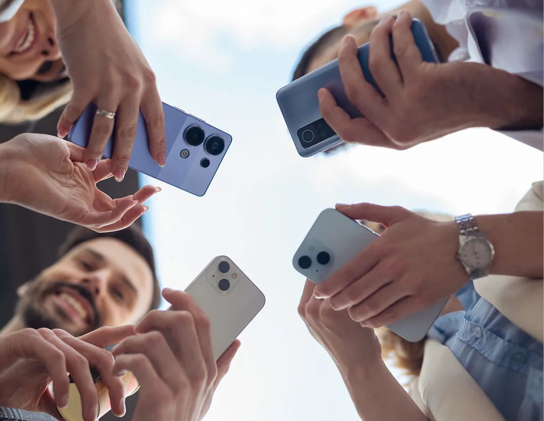 Group of people holding smartphones and looking down at the camera against a bright sky.