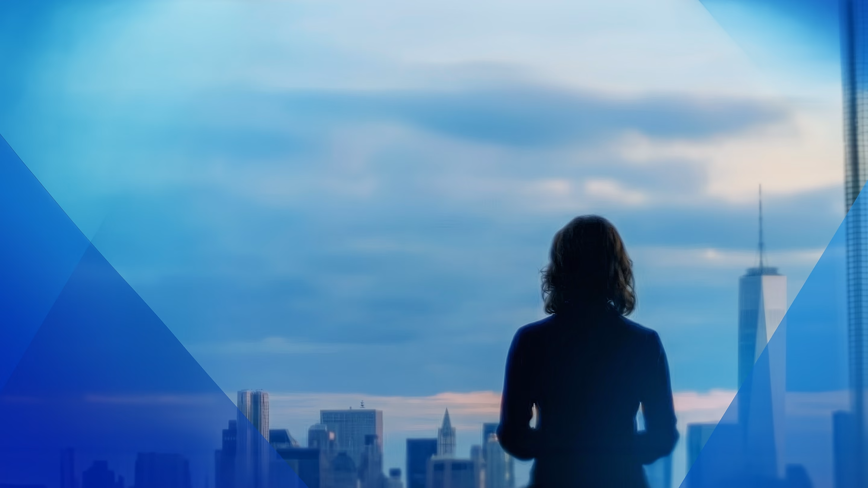 Person silhouette looking at city skyline at dusk with tall buildings and cloudy sky.