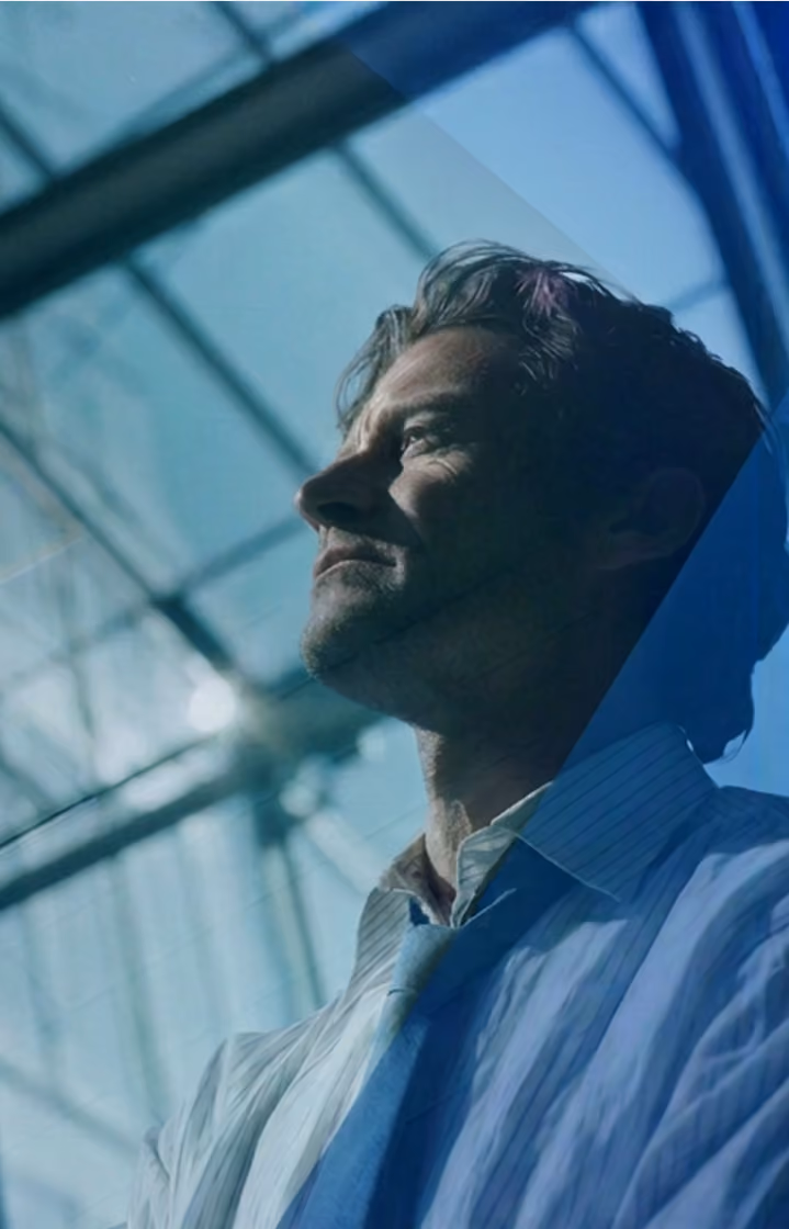 Man in a dress shirt and tie gazing thoughtfully upward indoors with glass ceiling above.