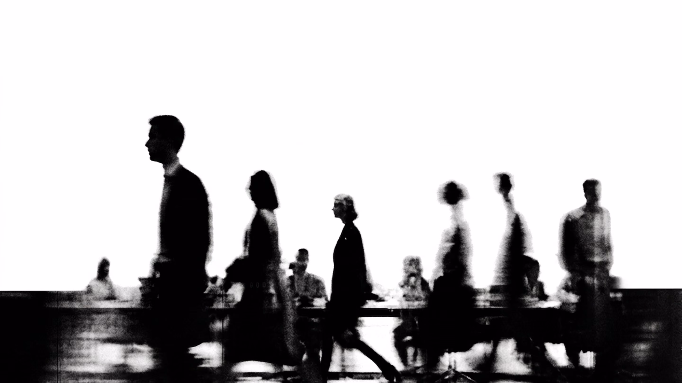 Black and white silhouette of people walking in front of seated figures at a table.