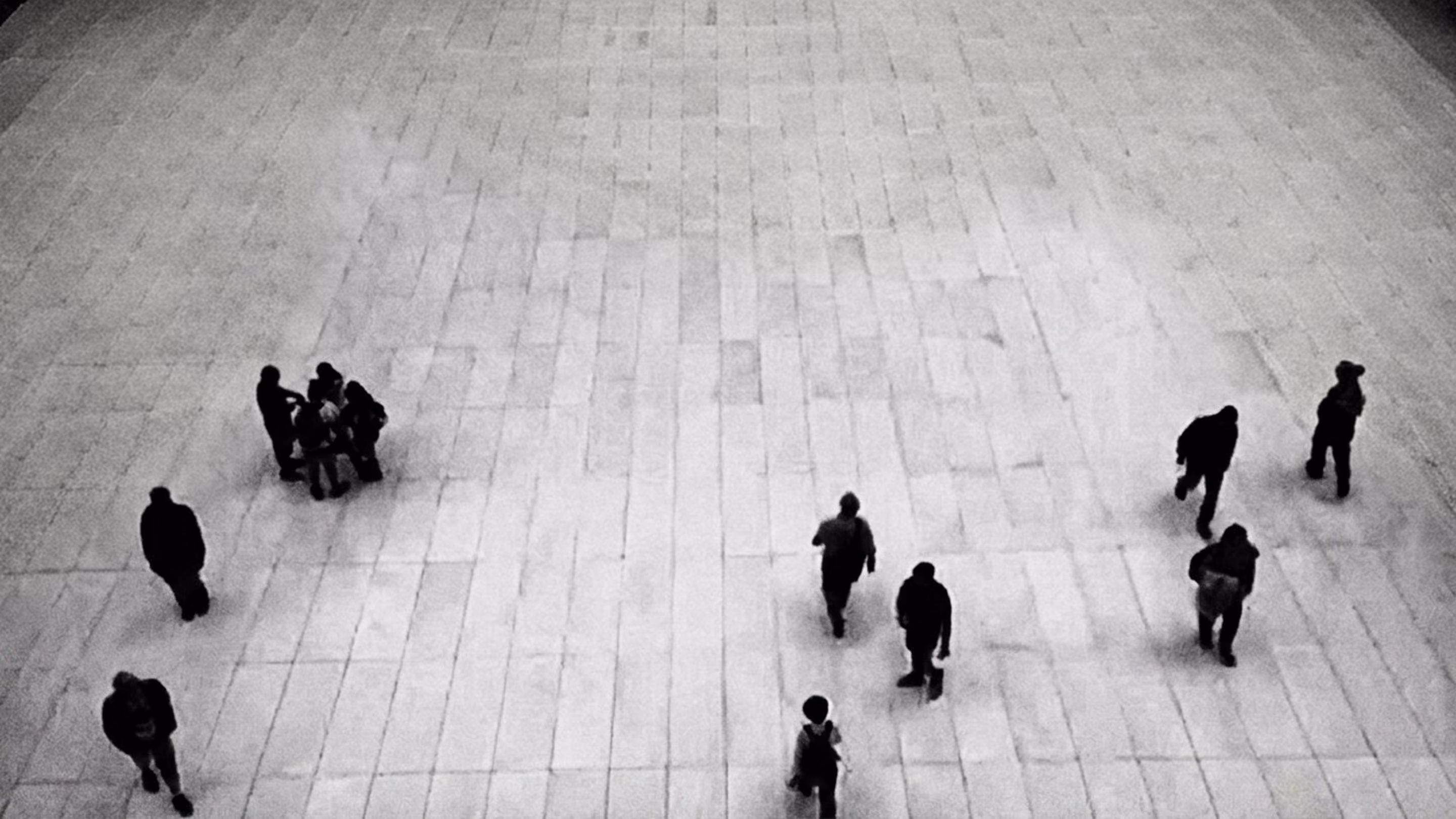 Black and white overhead view of people walking and standing on a large tiled floor.