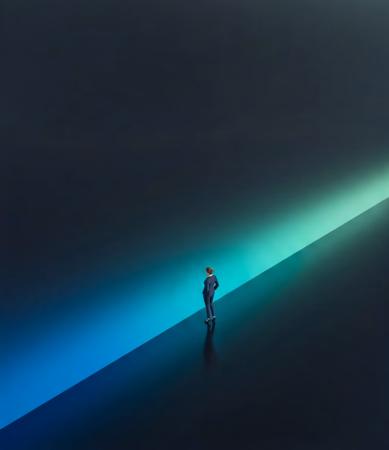 Person in a suit standing alone on a dark surface with a diagonal blue and green light beam.