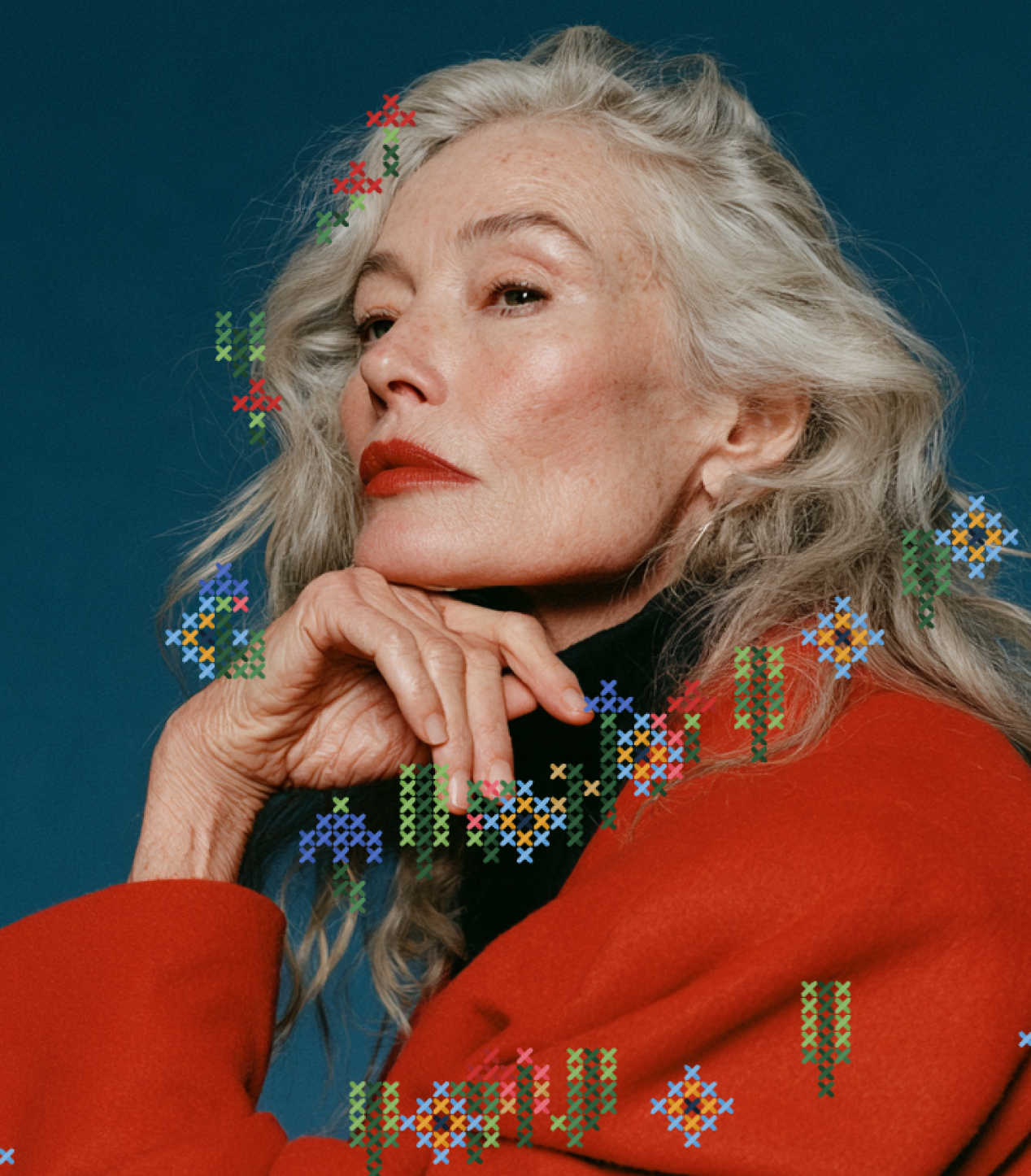 Close-up of a silver-haired woman in a red coat, with colourful cross-stitch flowers stitched over her hair and shoulders
