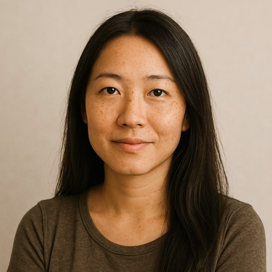 Portrait d'une femme asiatique aux cheveux longs noirs, portant un t-shirt marron, regardant directement la caméra avec une légère expression souriante sur un fond beige neutre.