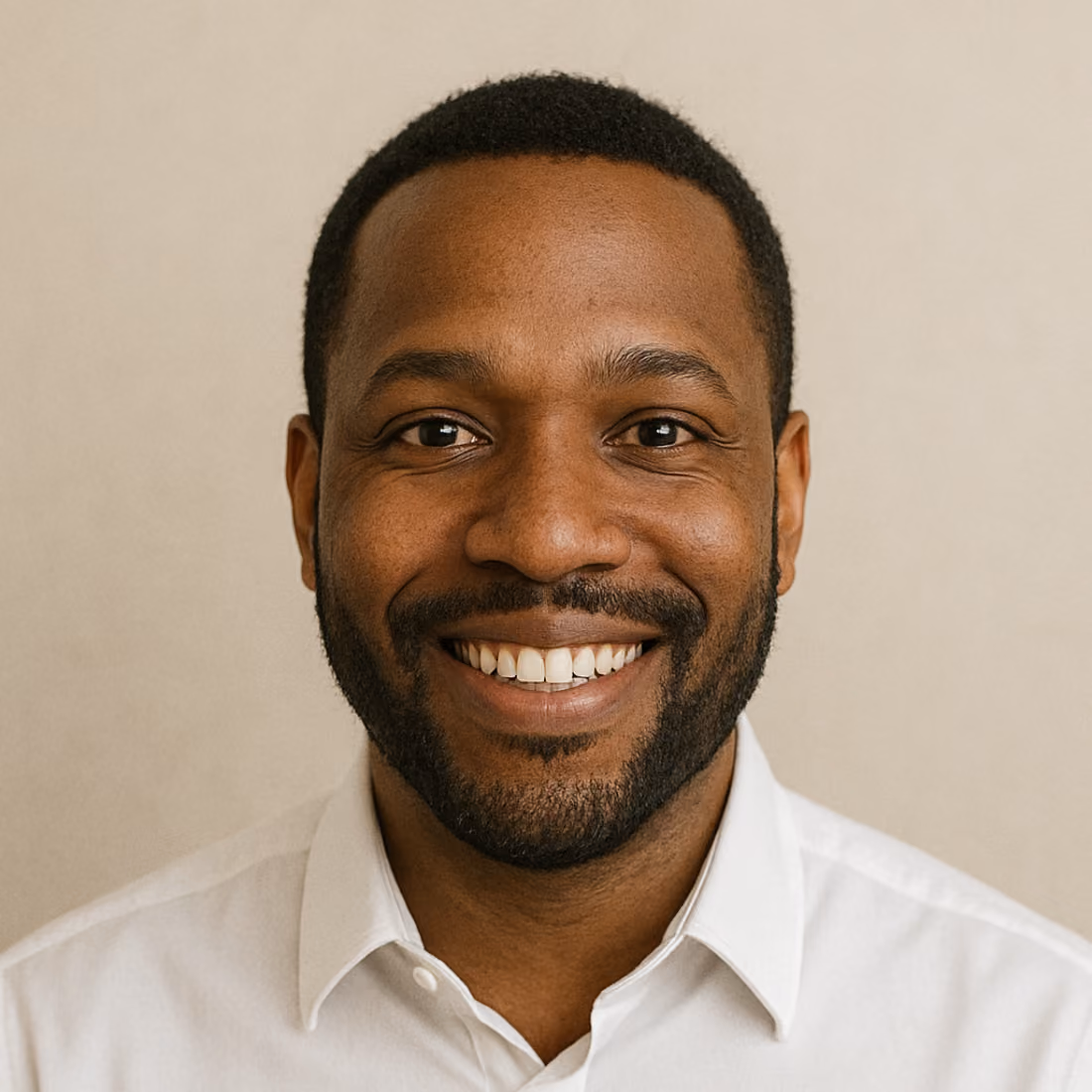 Portrait d'un homme souriant avec une barbe bien entretenue et une chemise blanche sur un fond beige neutre.