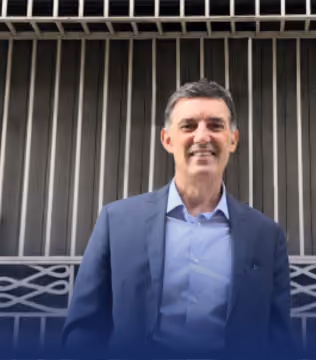 Homme souriant en costume bleu marine devant une façade à claire-voie