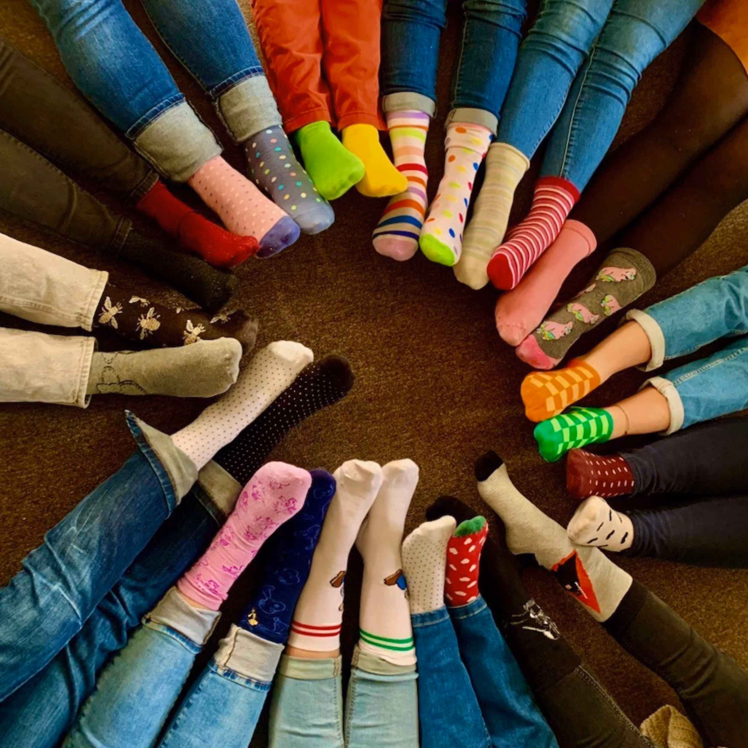 Un cercle formé par plusieurs personnes assises, montrant leurs pieds en chaussettes colorées et à motifs variés, avec des jeans et pantalons visibles.