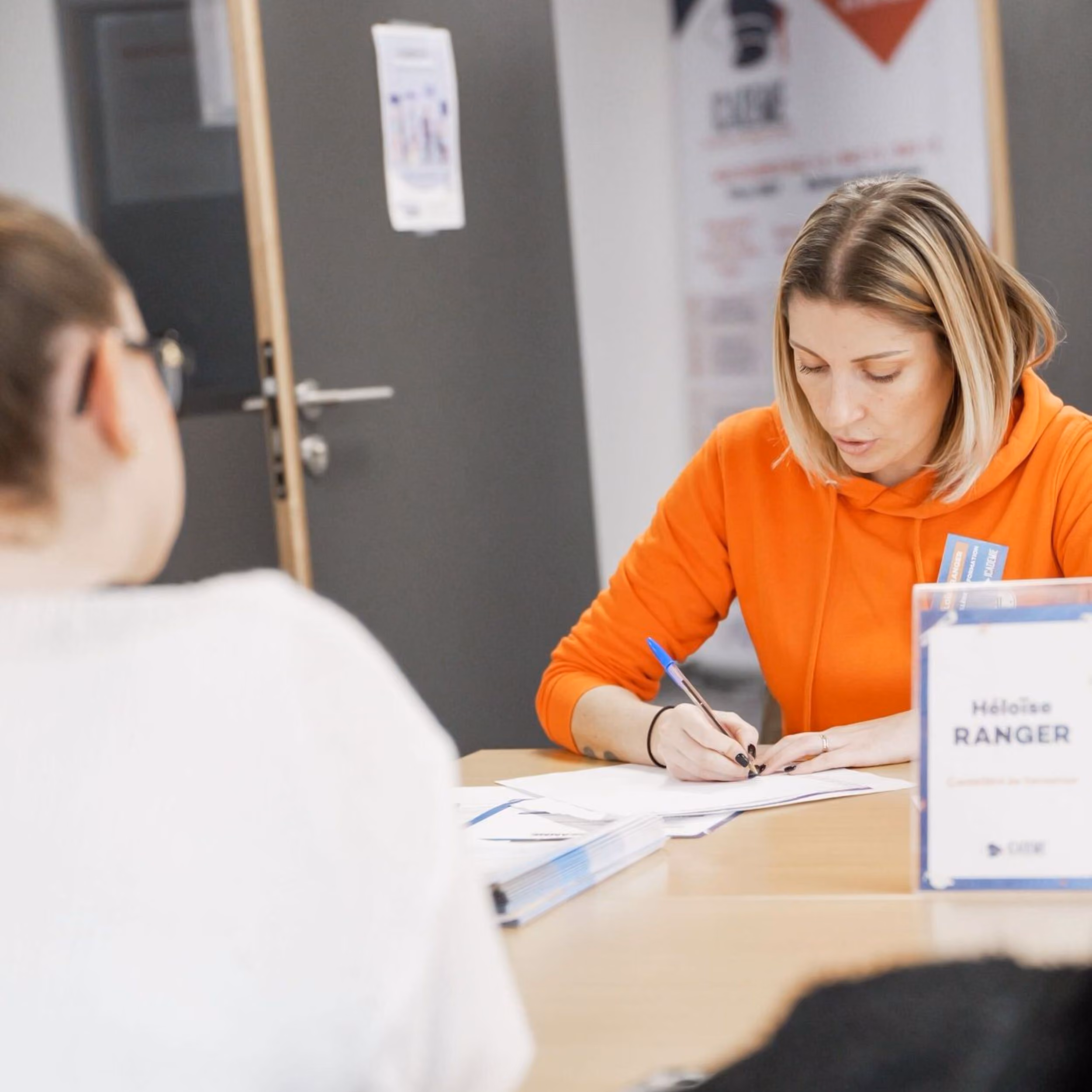 Conseillère Icademie en sweat orange remplissant un document face à une candidate