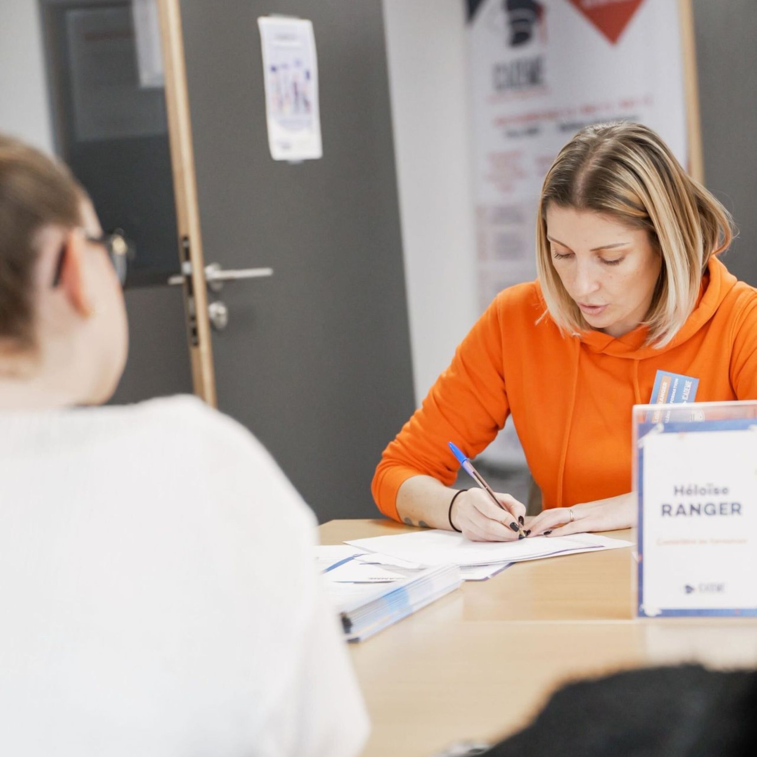 Conseillère Icademie en sweat orange remplissant un document face à une candidate