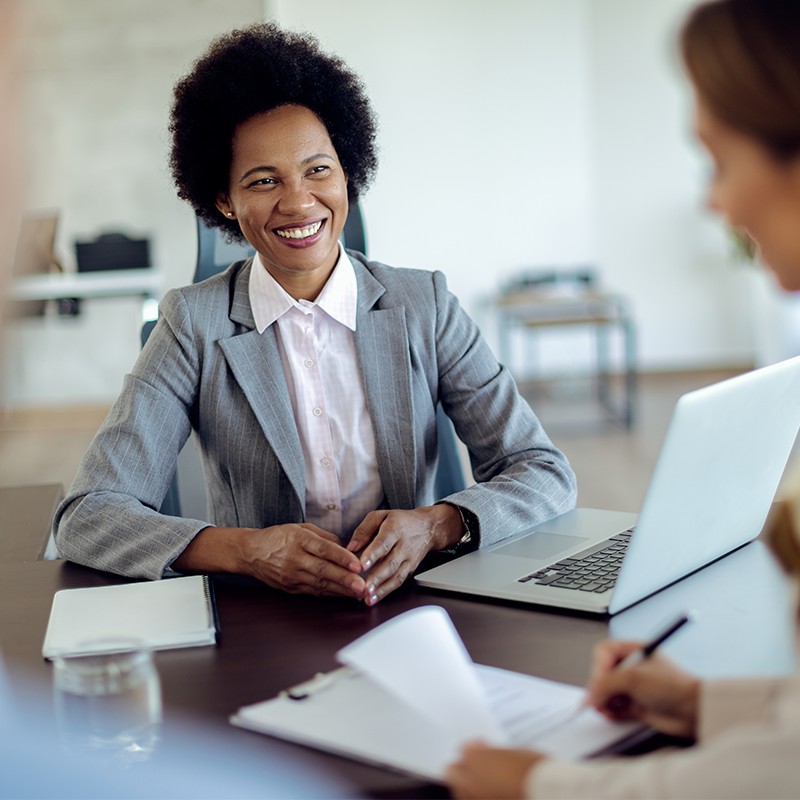 Conseillère souriante en veste grise recevant une cliente à son bureau