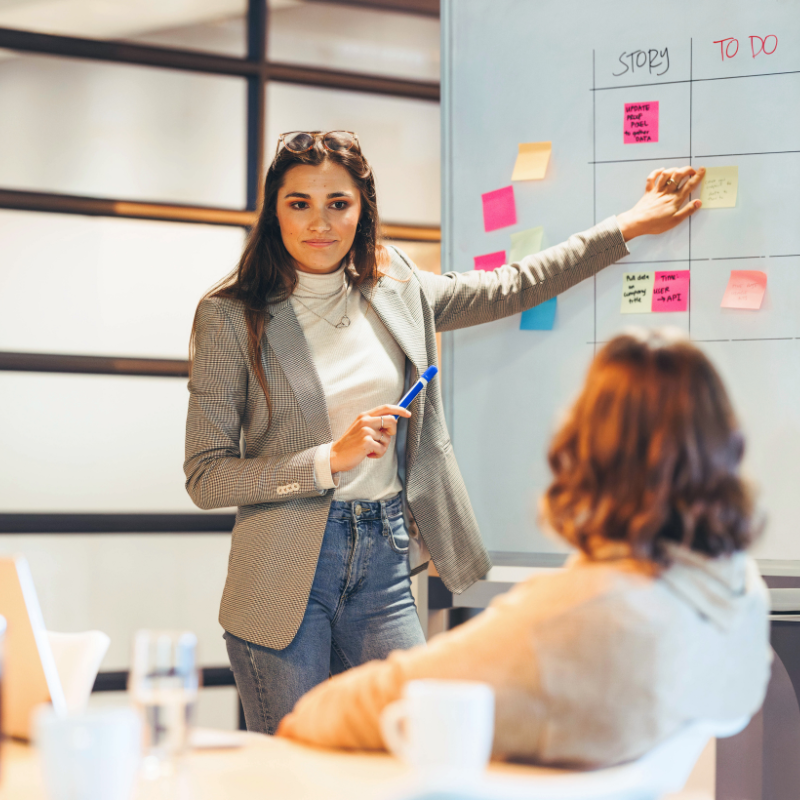 Femme animant une réunion devant un tableau de post-it story et to do
