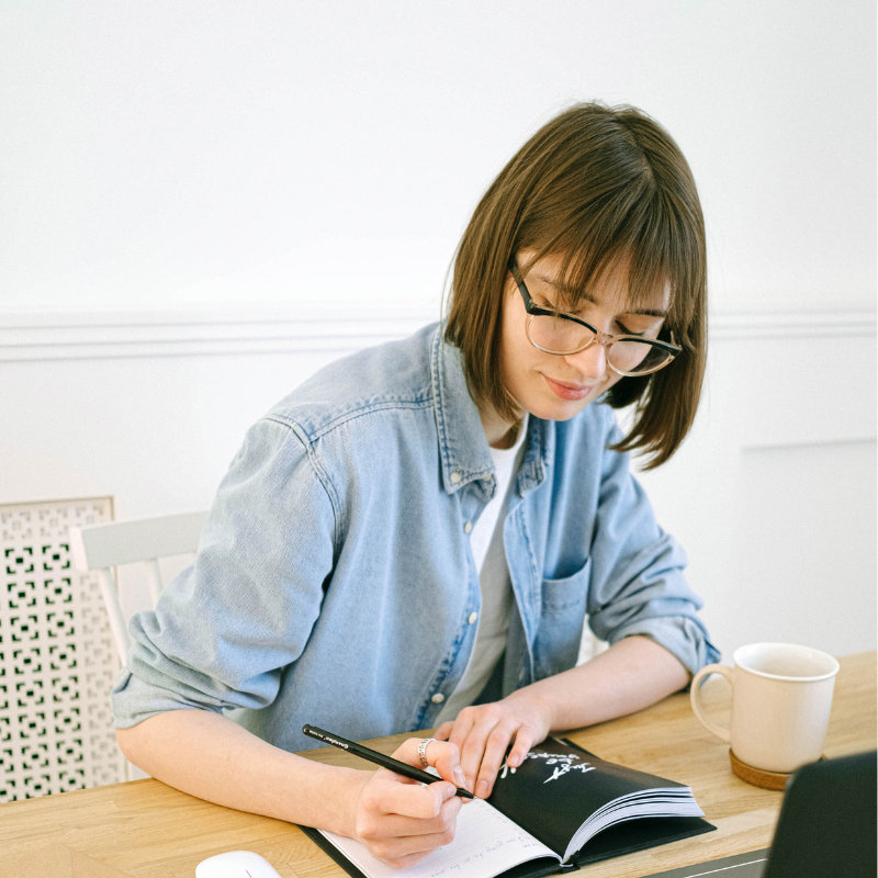 Jeune femme à lunettes écrivant dans un carnet à son bureau