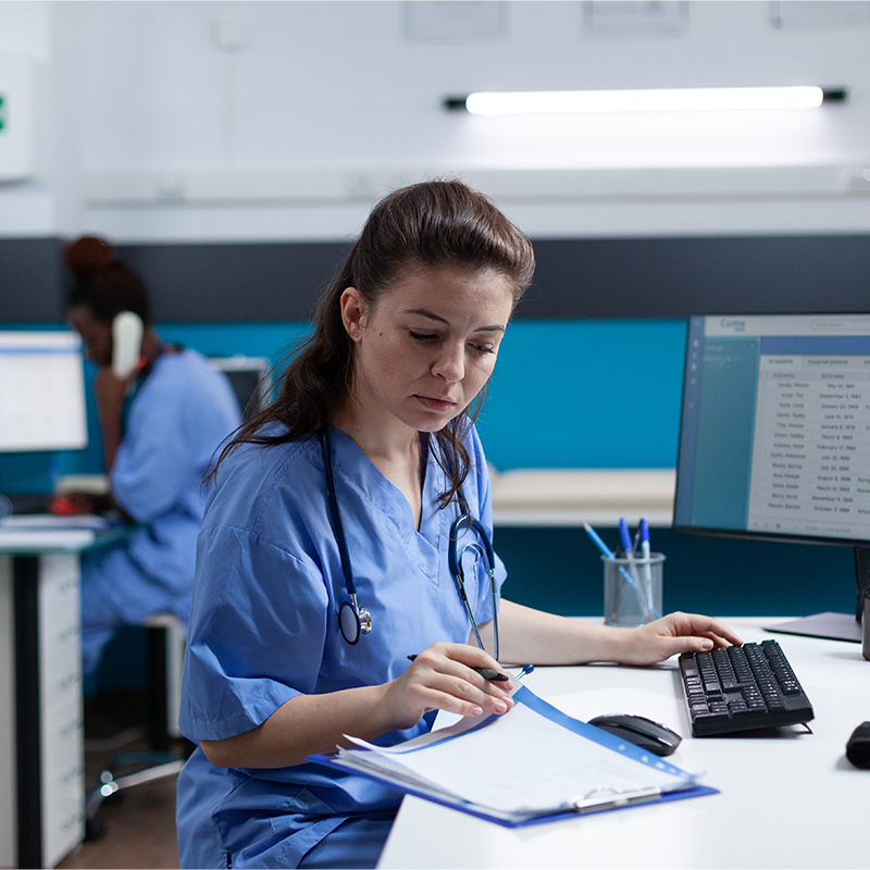 Secrétaire médicale en blouse bleue remplissant un dossier à l'accueil d'un cabinet