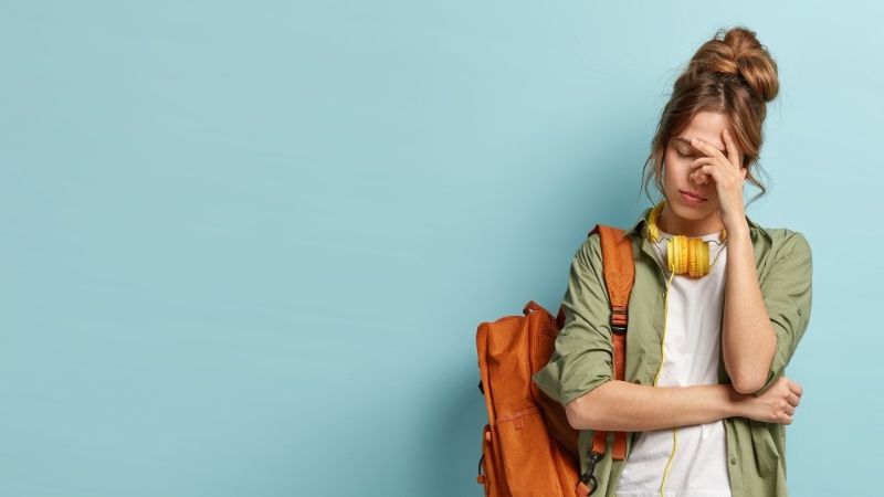 Jeune femme avec un sac à dos, main sur le front, l'air perplexe, sur fond bleu