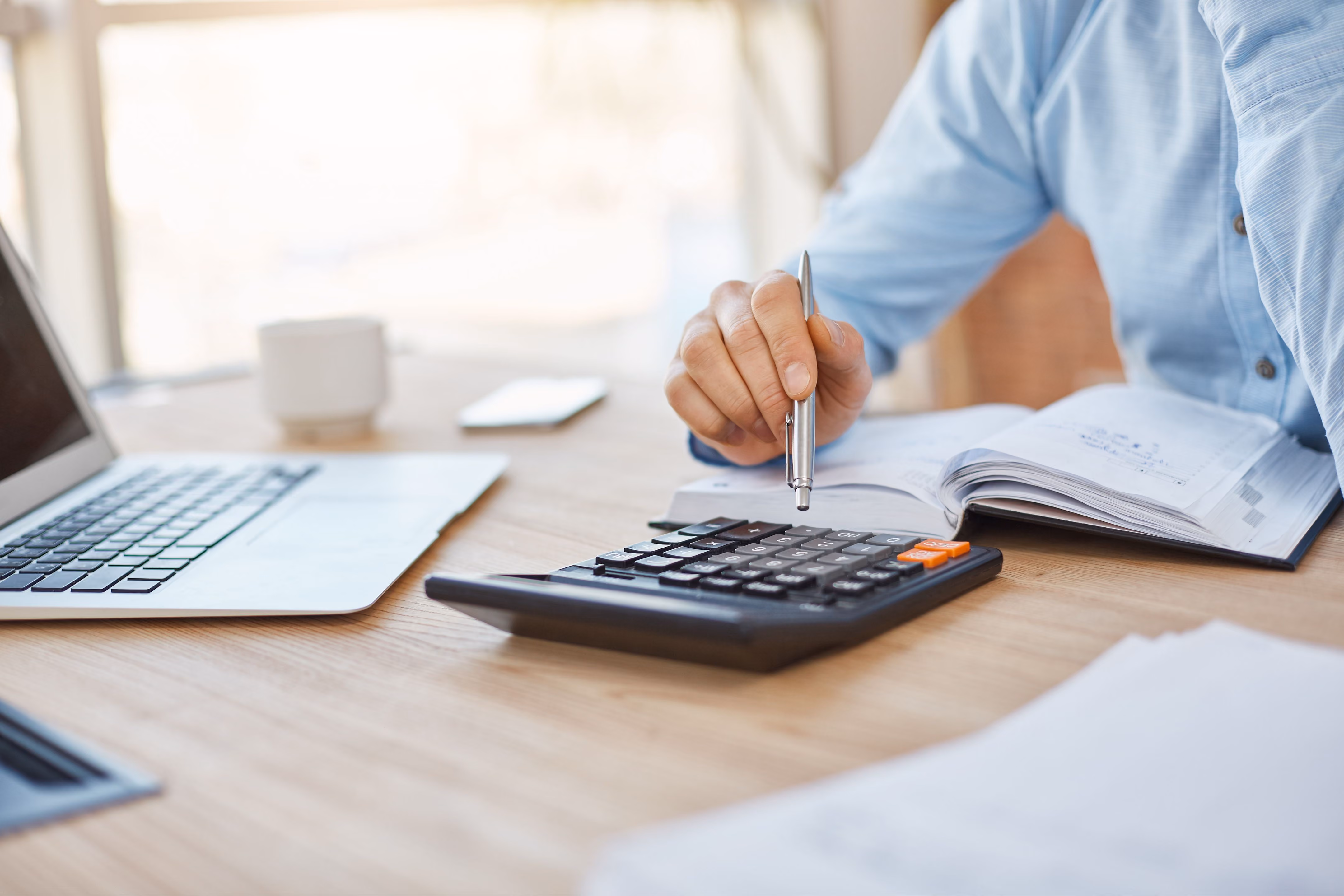 Main tapant sur une calculatrice à côté d'un carnet et d'un ordinateur portable