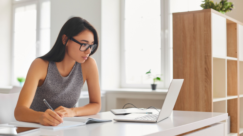 Étudiante à lunettes prenant des notes devant son ordinateur portable