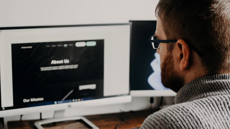 Homme barbu à lunettes regardant une page web sur un écran d'ordinateur