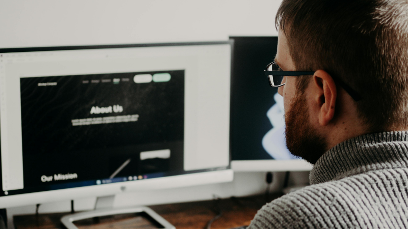 Homme barbu à lunettes regardant une page web sur un écran d'ordinateur