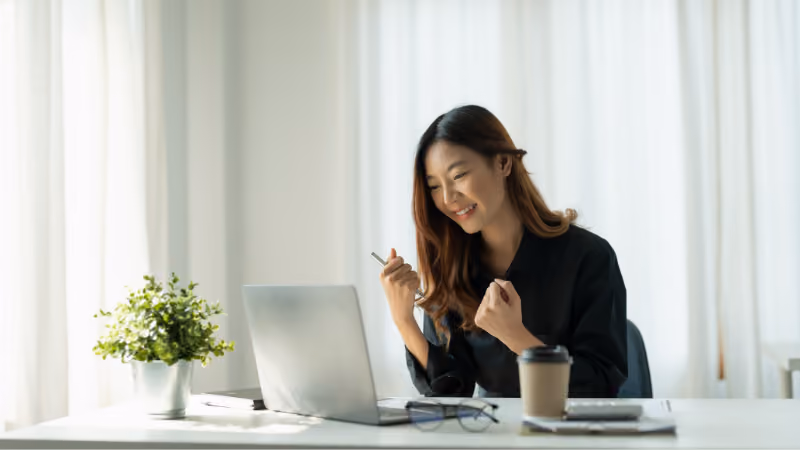 Jeune femme serrant les poings de satisfaction devant son ordinateur portable