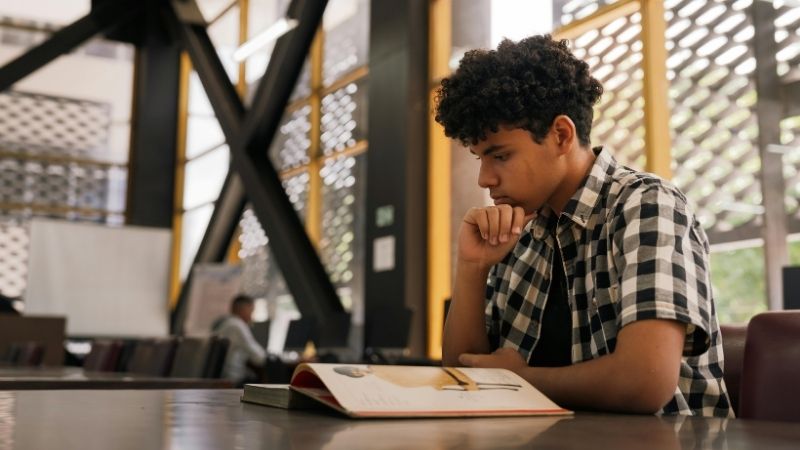 Jeune homme pensif lisant un livre à une table