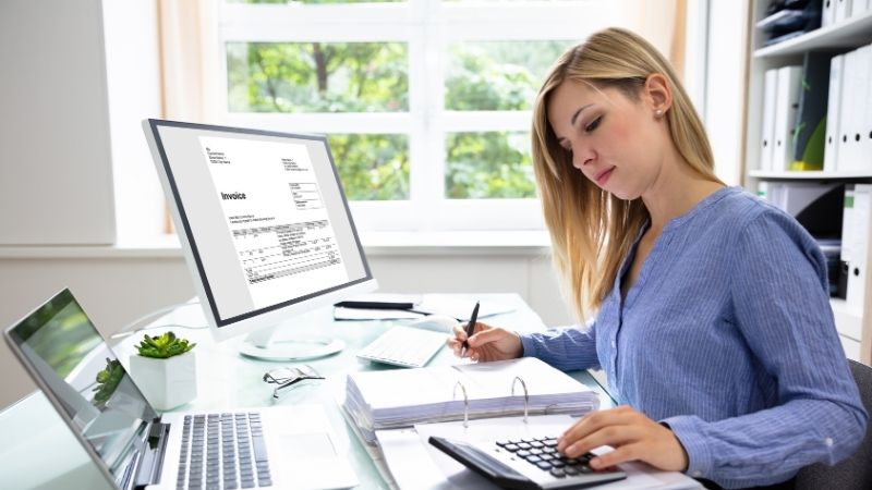 Comptable utilisant une calculatrice et prenant des notes devant son ordinateur