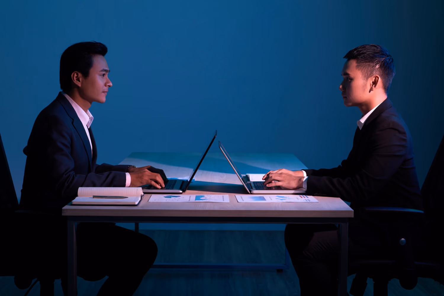 Deux hommes en costume face à face lors d'un entretien, ordinateurs ouverts