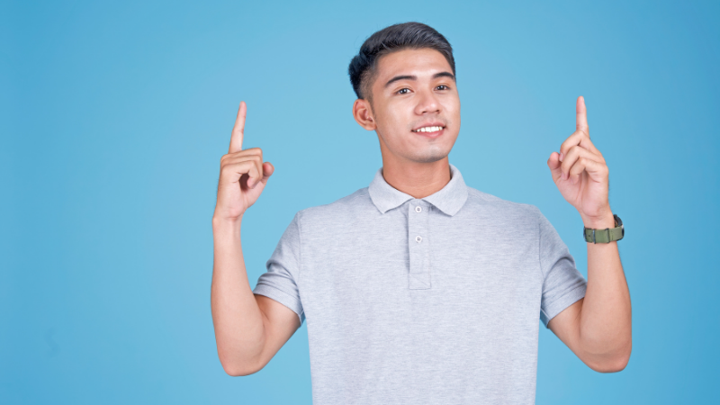 Jeune homme souriant pointant ses deux index vers le haut sur fond bleu