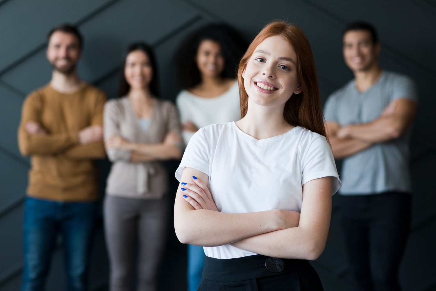 Jeune femme rousse souriante bras croisés devant une équipe de collègues