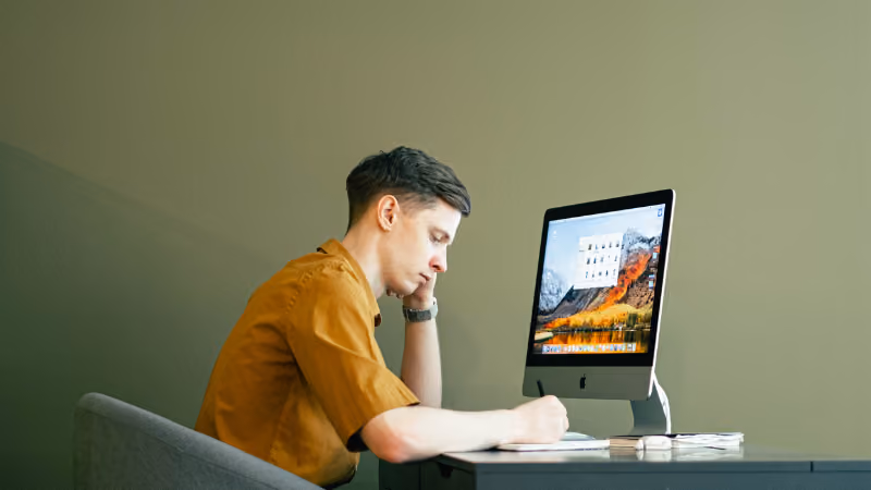 Jeune homme concentré prenant des notes devant un iMac
